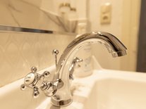 Elegante Waschbecken-Armatur im gold-weißen Bad der Suite Nachtigall im Schlössle Seeburg