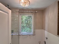 Elegantes Badezimmer der Suite Romantik mit Kristall-Deckenleuchte, großem Fenster und edlem Marmorboden.