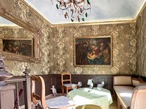 Eleganter Sitzbereich im Turmzimmer Luise der Suite Nachtigall mit Gemälde, Tisch und Sofa.