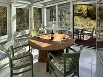 Wintergarten der Suite Nachtigall im Schloss Seeburg mit rundem Holztisch, vier Stühlen und Weingläsern, Blick auf die Terrasse.