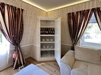 Wohnzimmer der Suite Nachtigall im Schloss Seeburg mit stilvollem Weinschrank, Gläsern und edlen Vorhängen.