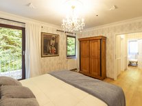 Schlafzimmer der Suite Romantik im Schlössle Seeburg mit Doppelbett, antikem Kleiderschrank und Kronleuchter.