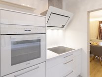 Moderne, helle Küche mit weißen Hochglanzfronten, Backoffen, Abzugzhaube, Blick ins Esszimmer.