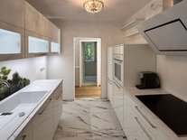 Moderne, helle Küche mit weißen Hochglanzfronten, Backoffen, Abzugzhaube, Blick ins Esszimmer.