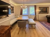 Helles Esszimmer mit Eckbank, TV, modernem Holztisch, Gemälden, Parkettboden und Kronleuchter.