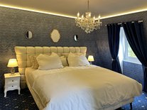 Schlafzimmer der Suite Nachtigall mit großem Bett, blauer Wandverkleidung und goldenen Spiegeln