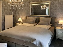 Doppelbett im zweiten Schlafzimmer der Suite Nachtigall mit Kronleuchter und Spiegelwand