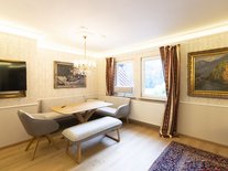 Helles Esszimmer mit Eckbank, TV, modernem Holztisch, Gemälden, Parkettboden und Kronleuchter.