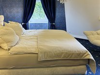 Doppelbett in der Suite Nachtigall im Schlössle Seeburg mit blauem Teppich und eleganter Einrichtung